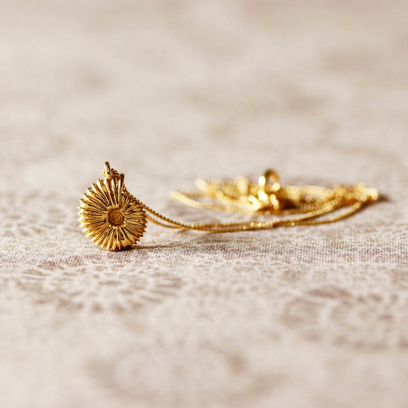 May include: A gold necklace with a round pendant that resembles a flower. The pendant has a textured, circular design.