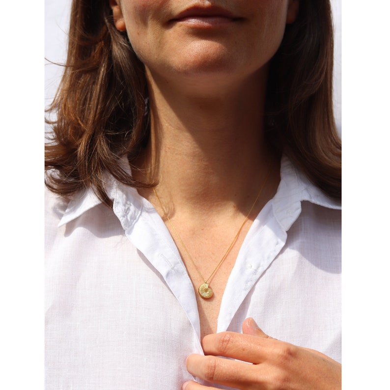 May include: A gold necklace with a small, round pendant. The pendant has a textured, sunburst design.