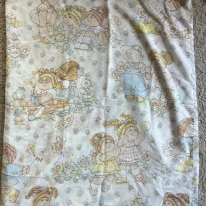 May include: White sheet featuring a repeating pattern of Cabbage Patch Kids in various poses. The illustrations include children with blonde and brown hair, wearing dresses and overalls, surrounded by flowers and butterflies.