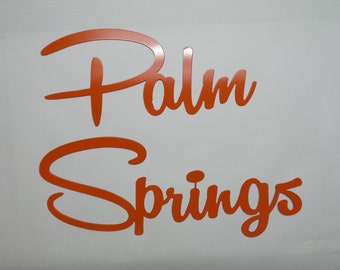 Könnte beinhalten: Orangefarbene kursive Schrift auf weißem Hintergrund mit der Aufschrift "Palm Springs".