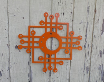 May include: Orange metal wall art with a geometric design featuring circles and lines. The art piece has a square shape with a circular opening in the center.