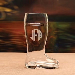 May include: A clear glass boot-shaped shot glass with a monogram of the letters "JFA" etched on the front.