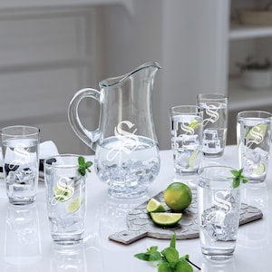 May include: A set of six clear glass tumblers and a pitcher, all with an etched letter 'S' design. The glasses are filled with ice and water, and there are lime slices on a cutting board.