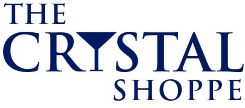 May include: The Crystal Shoppe logo in navy blue. The text is in a serif font, with the word "CRYSTAL" featuring a stylized crystal shape integrated into the letter "Y". The words "THE" and "SHOPPE" are above and below "CRYSTAL".