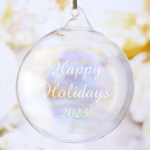 May include: Clear glass Christmas ornament with the text "Happy Holidays 2023" etched on the surface.