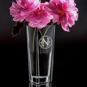 May include: A clear glass vase with a decorative etched letter N on the front. The vase is filled with pink flowers.