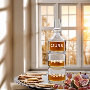 May include: A clear glass decanter with three sections, each labeled "OURS", "MINE", and "YOURS". The decanter is filled with a golden liquid and is sitting on a silver tray with crackers, cheese, grapes, and figs.