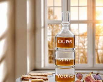 May include: A clear glass decanter with three sections, each labeled "OURS", "MINE", and "YOURS". The decanter is filled with a golden liquid and is sitting on a silver tray with crackers, cheese, grapes, and figs.