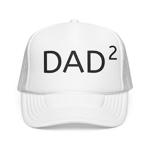 May include: White trucker hat with a curved brim and mesh back. The front of the hat features the word "DAD" in bold black letters, with a superscript "2" to the right, indicating a double dad or a dad of two.