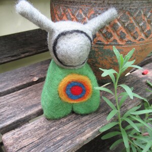 May include: A felt toy with long ears, a gray head with a black circle around the face, and a green body with a colorful target design.