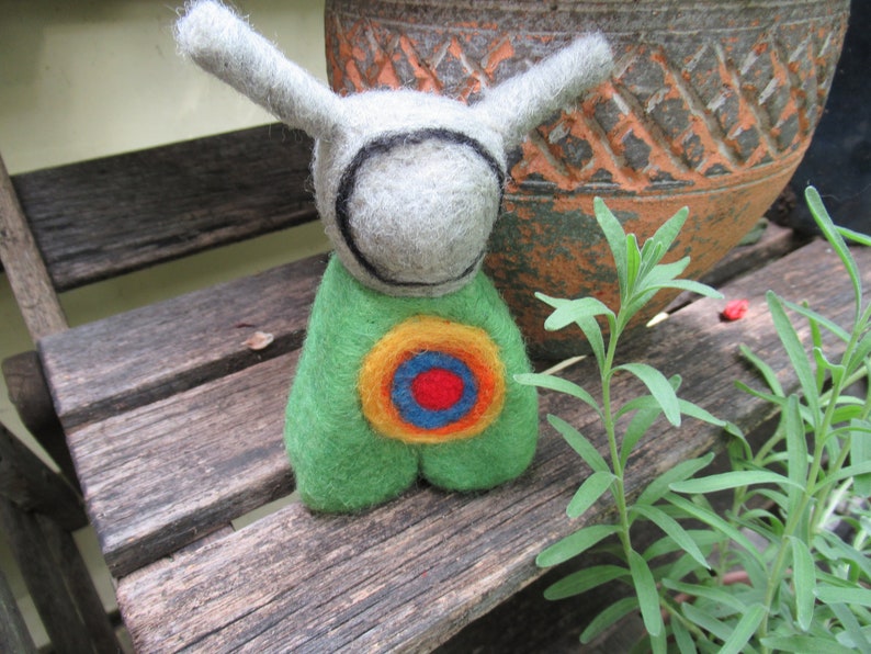 May include: A felt toy with long ears, a gray head with a black circle around the face, and a green body with a colorful target design.