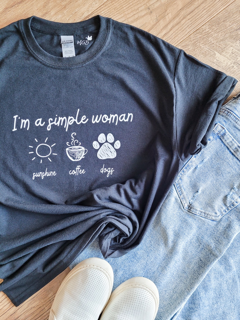 May include: A black t-shirt with the text "I'm a simple woman" and three icons: a sun, a coffee cup, and a paw print. The icons are labeled "sunshine", "coffee", and "dogs".