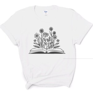 Peut inclure: T-shirt blanc avec une illustration en noir et blanc d'un livre ouvert avec des fleurs qui en sortent.