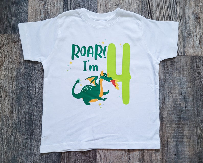 May include: White t-shirt with a green dragon and the text "Roar! I'm 4" printed on it.