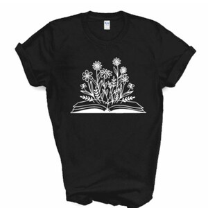 Peut inclure: T-shirt noir avec un motif blanc d'un livre ouvert avec des fleurs qui poussent.