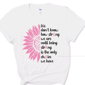 May include: A white short-sleeved t-shirt featuring a graphic of a pink sunflower on the left side and black text that reads: We don't know how strong we are until being strong is the only choice we have, with pink ribbons replacing the letter o.