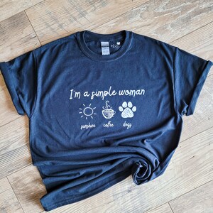 May include: A dark blue t-shirt with the text "I'm a simple woman sunshine coffee dogs" in white lettering. The shirt features a sun, a cup of coffee, and a paw print.