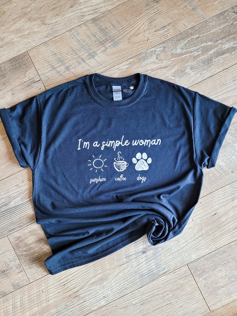 May include: A dark blue t-shirt with the text "I'm a simple woman sunshine coffee dogs" in white lettering. The shirt features a sun, a cup of coffee, and a paw print.