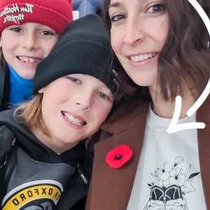 K&ouml;nnte beinhalten: Eine Frau und zwei Jungen l&auml;cheln f&uuml;r ein Foto. Die Frau tr&auml;gt einen braunen Mantel mit einer roten Mohnblumennadel und ein wei&szlig;es T-Shirt mit einem Hockeyschuh-Design und dem Text "Hockey Mom". Der Junge links tr&auml;gt eine rote M&uuml;tze mit dem Text "Tim Horton's" und ein blaues Hemd. Der Junge rechts tr&auml;gt eine schwarze M&uuml;tze und einen schwarzen und grauen Hoodie mit einem gelben und grauen Logo, auf dem "Oxford" steht.