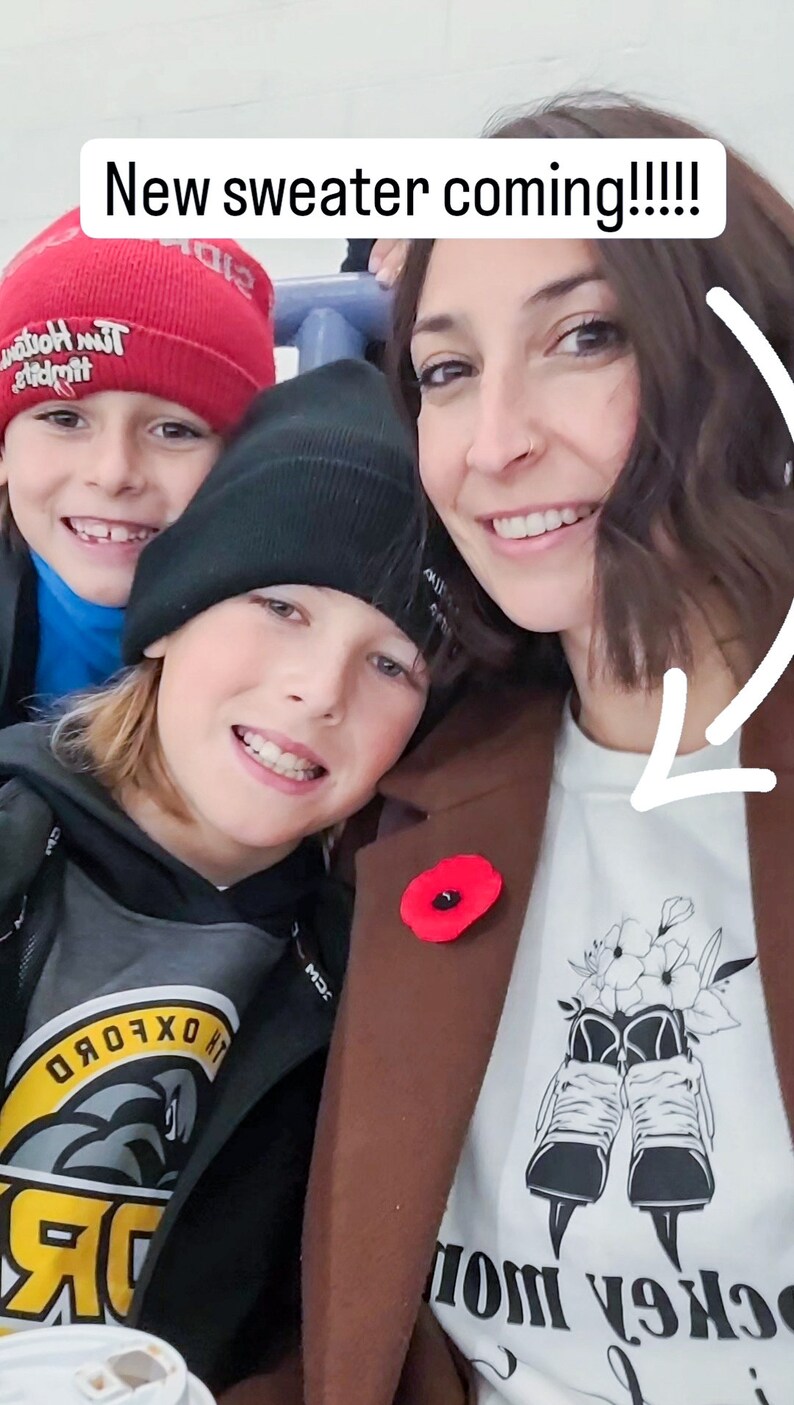 K&ouml;nnte beinhalten: Eine Frau und zwei Jungen l&auml;cheln f&uuml;r ein Foto. Die Frau tr&auml;gt einen braunen Mantel mit einer roten Mohnblumennadel und ein wei&szlig;es T-Shirt mit einem Hockeyschuh-Design und dem Text "Hockey Mom". Der Junge links tr&auml;gt eine rote M&uuml;tze mit dem Text "Tim Horton's" und ein blaues Hemd. Der Junge rechts tr&auml;gt eine schwarze M&uuml;tze und einen schwarzen und grauen Hoodie mit einem gelben und grauen Logo, auf dem "Oxford" steht.