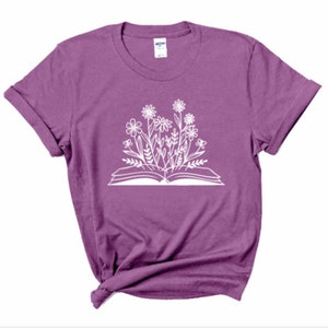 Peut inclure: Un t-shirt violet avec un imprim&eacute; blanc d'un livre ouvert avec des fleurs qui poussent.