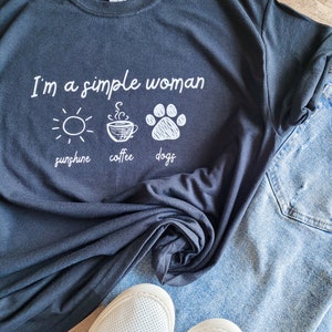 May include: A black t-shirt with the text "I'm a simple woman" and three icons: a sun, a cup of coffee, and a paw print. The icons are labeled "sunshine", "coffee", and "dogs".