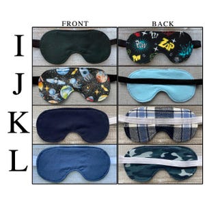 May include: A collection of four sleep masks labeled I, J, K, and L. Mask I features a black front and a comic book print back. Mask J has a space-themed front and a light blue back. Mask K is navy blue with a plaid back. Mask L is blue with a camo back.