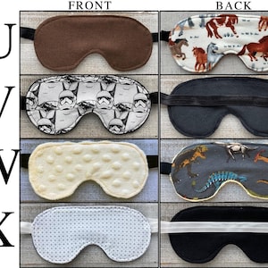 May include: A grid of four sleep masks labeled U, V, W, and X. Row U shows a solid brown front and a horse-patterned back. Row V shows a black and white Stormtrooper-patterned front and a solid black back. Row W shows a cream-colored textured front and a dinosaur-patterned back. Row X shows a white patterned front and a solid black back.