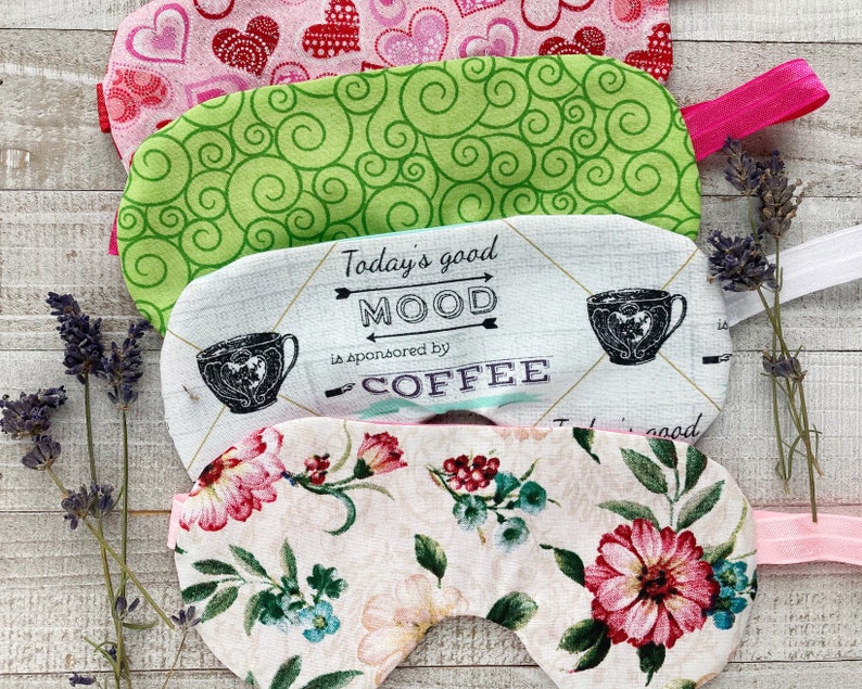 May include: Four fabric sleep masks with elastic bands. The masks feature various patterns, including hearts, green swirls, floral designs, and a coffee-themed print with the text "Today's good MOOD is sponsored by COFFEE."