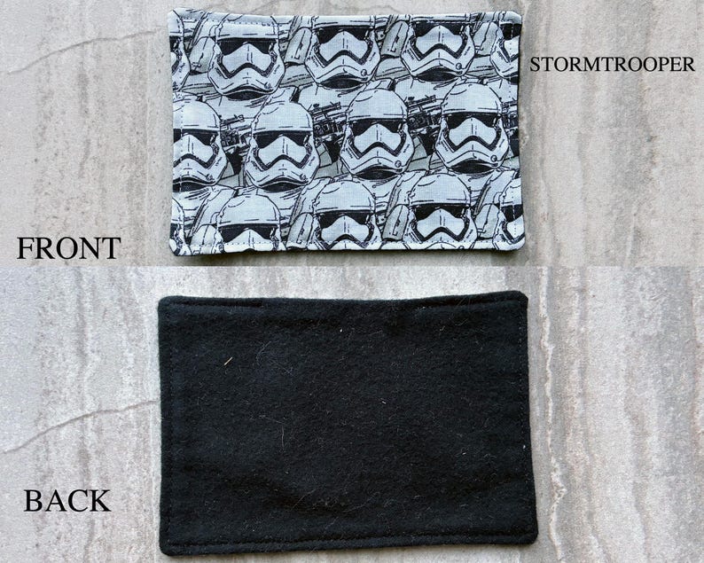 May include: A rectangular fabric patch featuring a repeating black and white pattern of Stormtrooper helmets. The front side displays the graphic print with the text STORMTROOPER, while the back side is a solid, plain black fabric material.