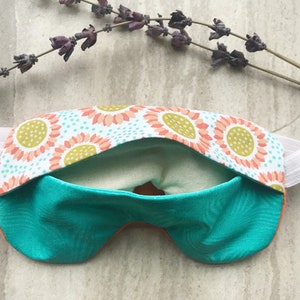 May include: A turquoise sleep mask with a floral pattern on the back. The mask has an elastic band for a comfortable fit.