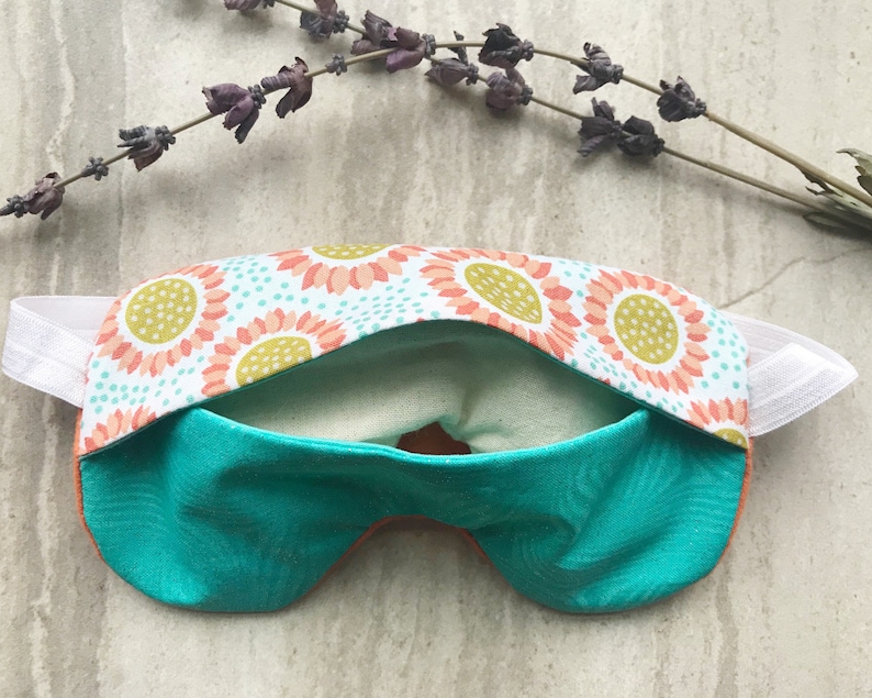 May include: A turquoise sleep mask with a floral pattern on the back. The mask has an elastic band for a comfortable fit.
