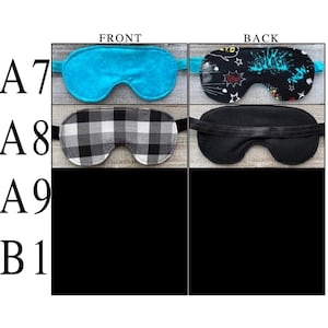 May include: Two sleep masks labeled A7 and A8. A7 features a solid turquoise front and a black back with a colorful comic-style splash print. A8 displays a black and white buffalo plaid front and a solid black back. Both include elastic straps.