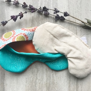 May include: A turquoise and orange sleep mask with a floral pattern and a white cotton insert. The mask is made of soft fabric and has an elastic strap.