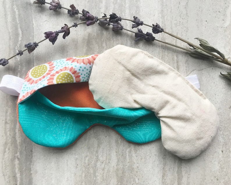 May include: A turquoise and orange sleep mask with a floral pattern and a white cotton insert. The mask is made of soft fabric and has an elastic strap.