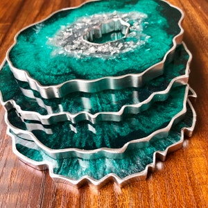 May include: Set of four green and silver agate-shaped coasters with a silver rim. The coasters are stacked on top of each other.