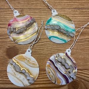 May include: Four round, white, resin Christmas ornaments with gold glitter and white stones. Each ornament has a different color swirl pattern: pink, green, white, and purple.