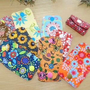 May include: Nine colourful fabric keychains with different patterns and buttons. The keychains are made of fabric with floral, geometric and abstract designs.