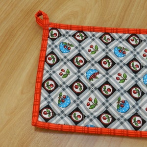 May include: Red and white quilted hot pad with a cherry and bowl pattern. The hot pad has a loop for hanging.