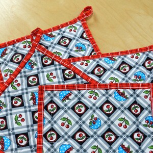 May include: Set of four red and white quilted pot holders with a black and white checked pattern and a cherry design.
