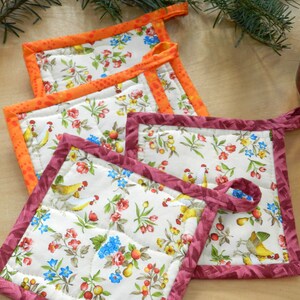 May include: Four quilted pot holders with a floral pattern and a rooster design. The pot holders have orange, burgundy, and white trim.