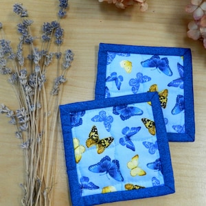 May include: Two blue quilted pot holders with a blue trim and a butterfly pattern. The butterflies are yellow and blue on a light blue background.