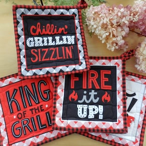 May include: Four red and black checkered pot holders with different sayings. The sayings are "Chillin' Grillin' Sizzlin'," "King of the Grill," "Fire it Up!" and "Grill Master."