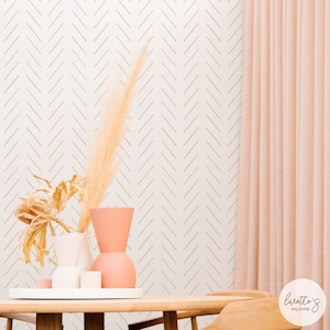 May include: A white wallpaper with a subtle herringbone pattern in a light brown colour. The wallpaper is shown in a room with a table and a vase with dried pampas grass. The text "lurette's wallpaper" is in the bottom right corner of the image.