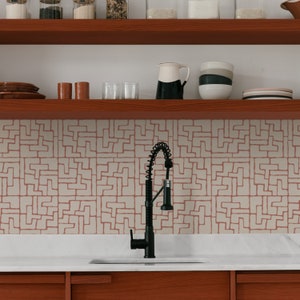 Peut inclure: Un robinet de cuisine noir avec un pulvérisateur extractible est installé au-dessus d'un plan de travail blanc. La crédence est en carrelage rose clair avec un motif géométrique blanc.