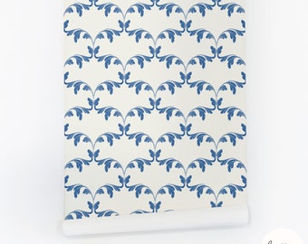 May include: A roll of wallpaper featuring a repeating pattern of blue stylized leaves on a cream background. The leaves are arranged in a symmetrical, curved design. The bottom edge of the roll is unrolled, revealing the paper's texture. The brand name "luette's wallpaper" is visible.