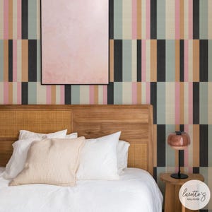 May include: A bedroom with a wooden headboard, white bedding, and a patterned wallpaper. The wallpaper features vertical stripes in black, pink, beige, and teal. A pink framed artwork hangs above the bed. A small lamp sits on a wooden side table.