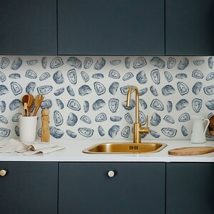 May include: A kitchen sink with a gold tap and a white worktop. The backsplash is a white tile with a blue and white oyster pattern.