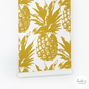 May include: A roll of wallpaper featuring a repeating pattern of large, golden-yellow pineapples on a white background. The pineapple design has a textured, brushstroke appearance. The bottom right corner shows the brand name "Luvette's Wallpaper".