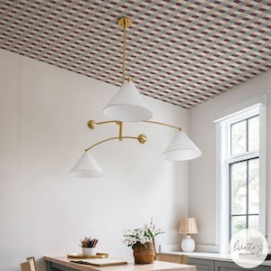 May include: A room featuring a patterned ceiling with a grid design in shades of red, beige, and blue. A gold chandelier with three white cone-shaped lamps hangs from the ceiling. A table with a basket of flowers and a lamp are visible.